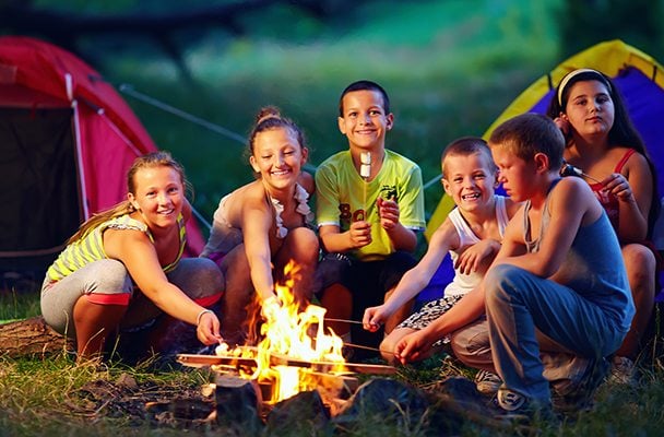 Kids roasting marshmallows over fire near tents