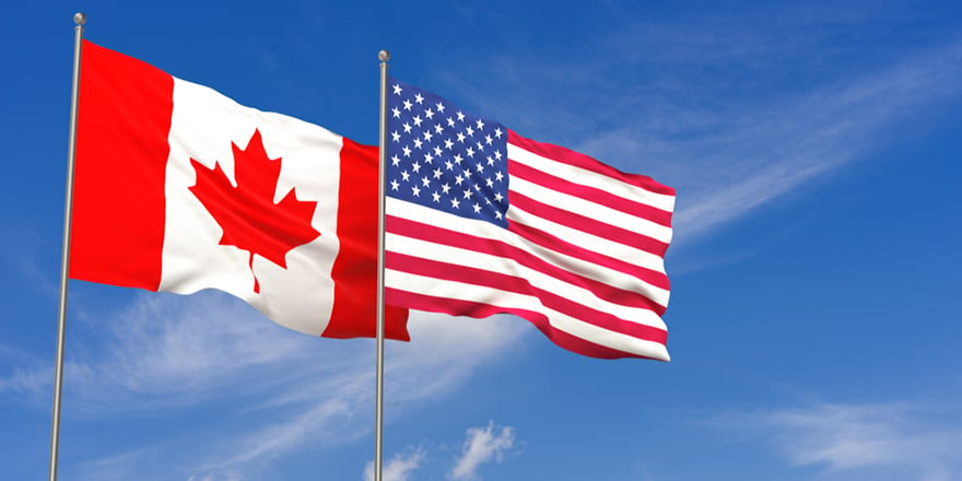 Canadian and American flags flying in blue sky