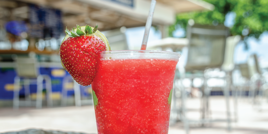 Frozen strawberry daiquiri in glass with strawberry on the rim and straw