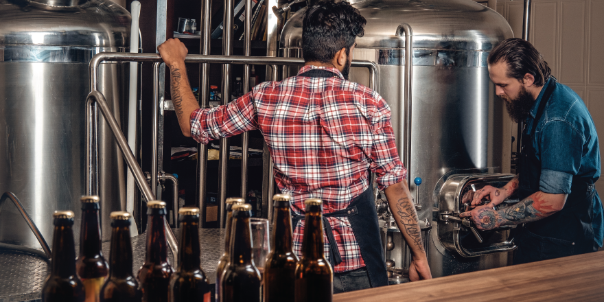 Two men working at large silver containers in brewery