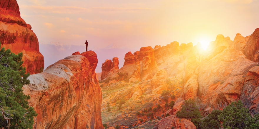 person standing on top of mountain with sun setting