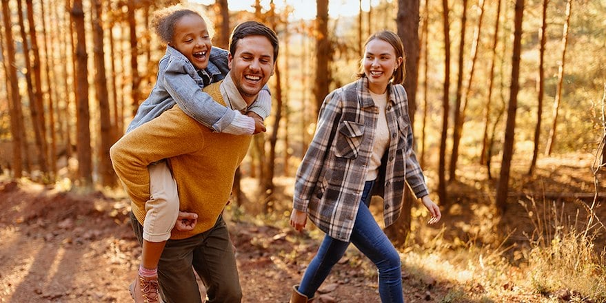 Man and woman walking in woods. Man is carrying child on his back.